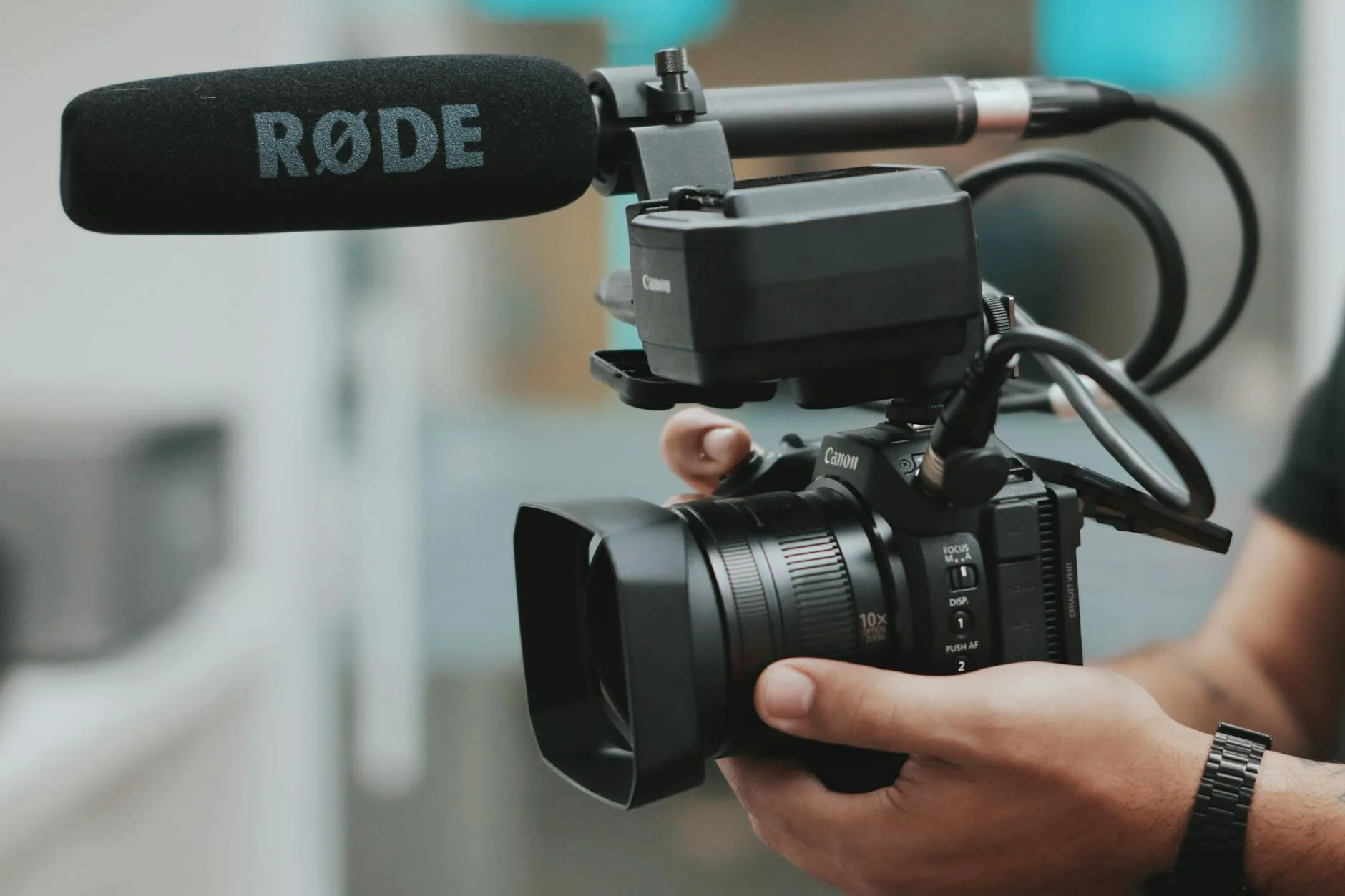 Hands holding a professional video camera with a RØDE microphone for a corporate shoot.