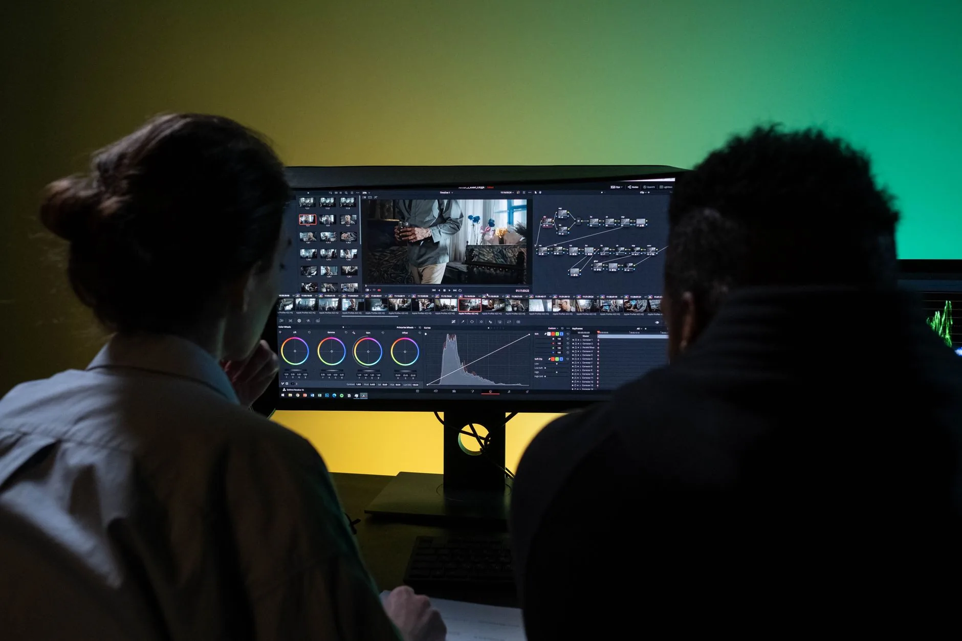 Equipo de dos profesionales revisando edición de vídeo en una mesa con dos monitores