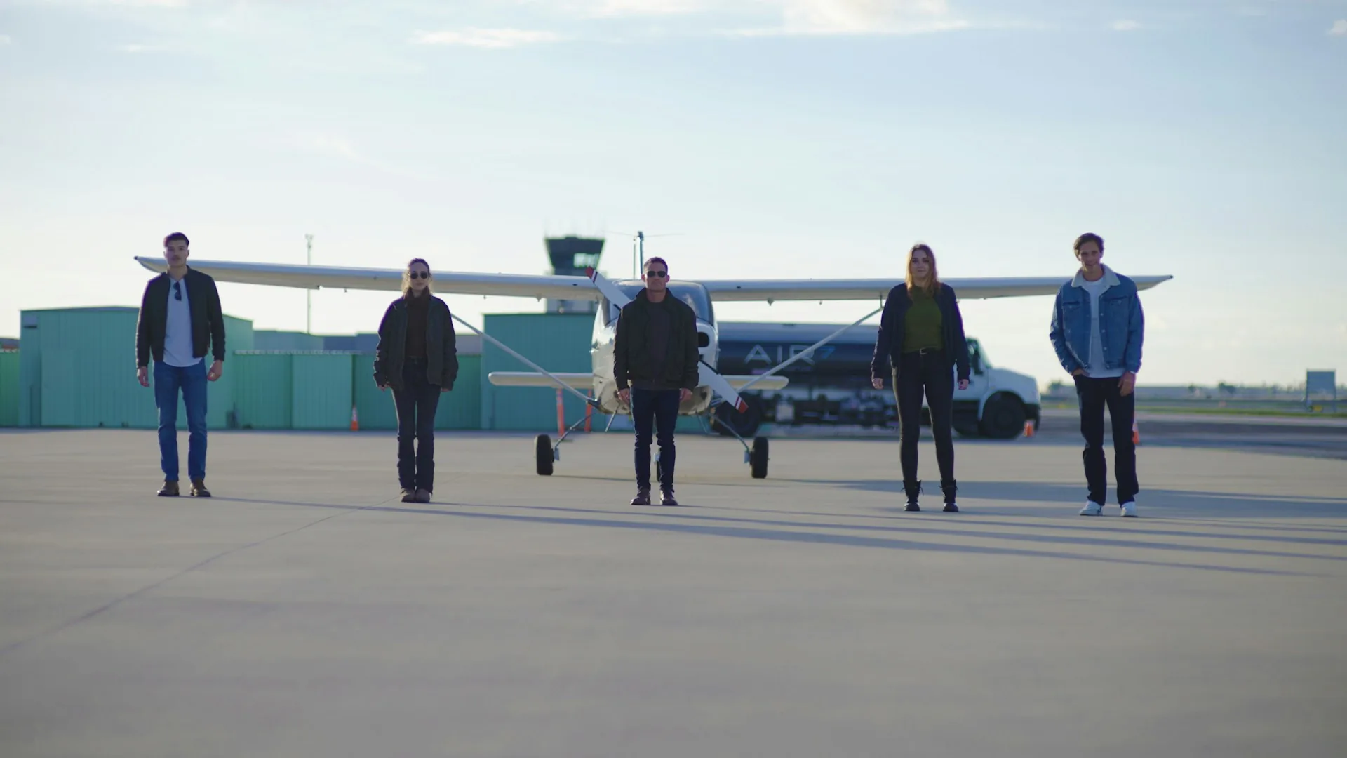 Equipo de producción de vídeo esperando en pista junto a una avioneta antes de viajar a la siguiente sede