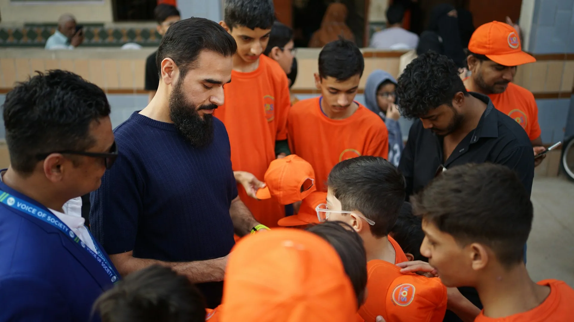 Volunteer handing out orange hats to children during a charity activity