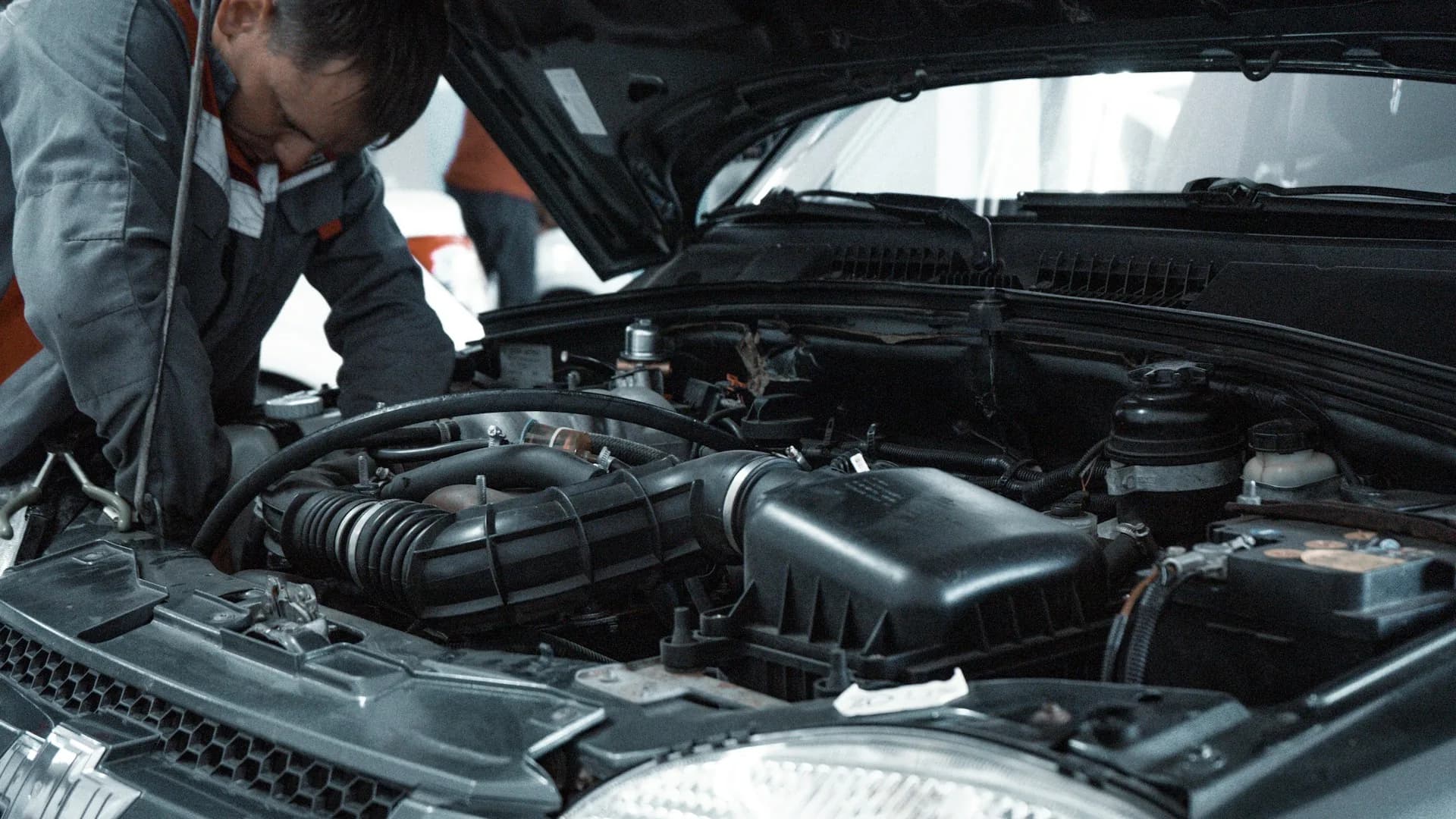 Mechanic inspecting a vehicle's engine with the hood open in a workshop