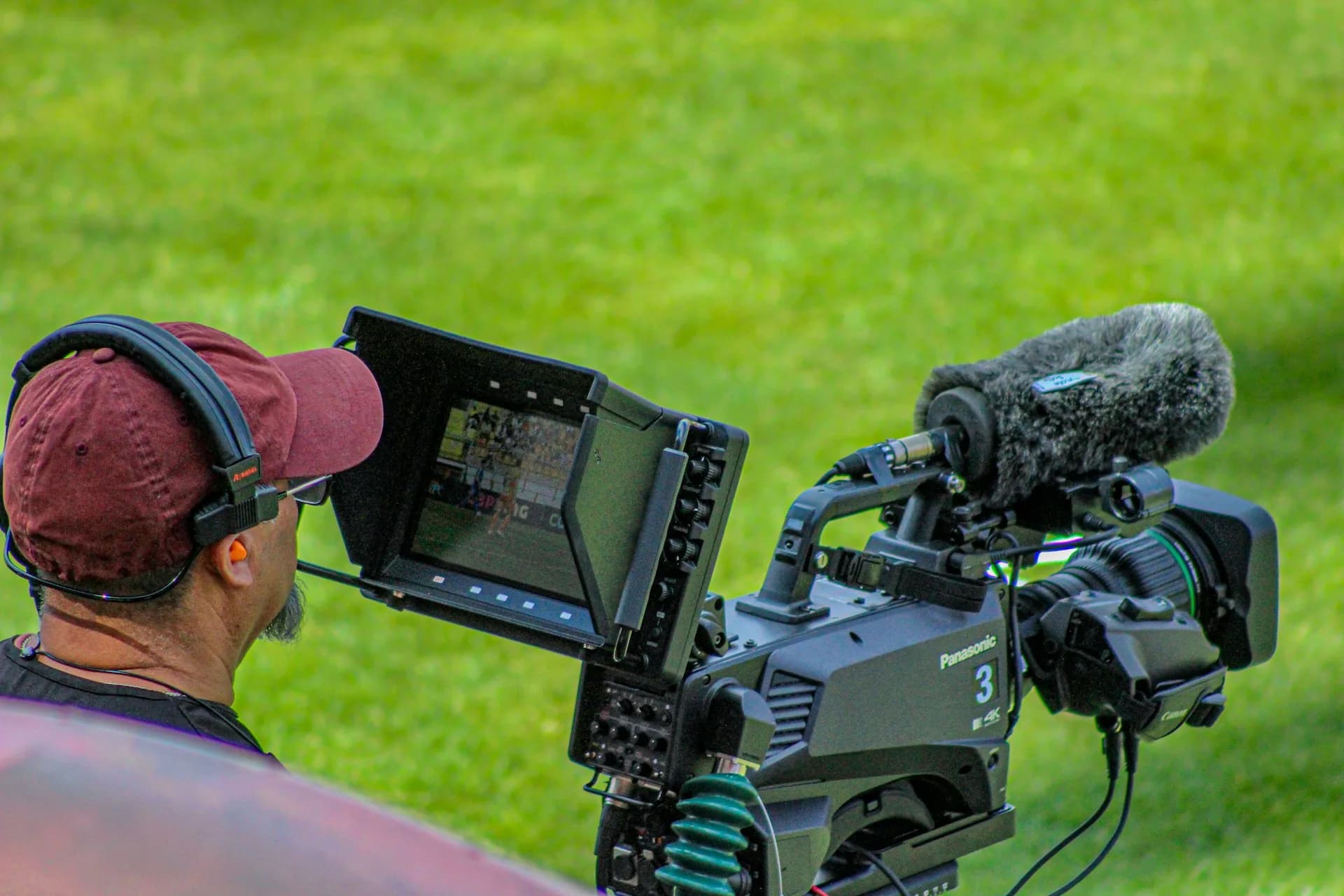 Cámara de televisión Panasonic con micrófono de pértiga grabando en un campo de césped